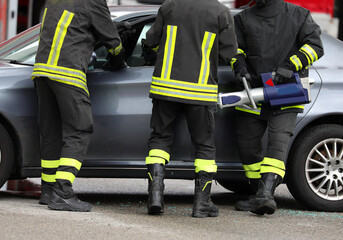 Three firefighters use a powerful hydraulic retractor called jaws OF LIFE to open car door after traffic accident