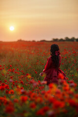 Beautiful girl with black hair and short red dress posing in poppy field of flowers.
