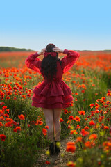 Beautiful girl with black hair and short red dress posing in poppy field of flowers.