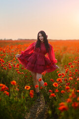Beautiful girl with black hair and short red dress posing in poppy field of flowers.