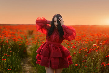 Beautiful girl with black hair and short red dress posing in poppy field of flowers.