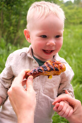 Laughing toddler outdoors with grilled chicken drumstick at picnic