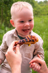 Laughing toddler outdoors with grilled chicken drumstick at picnic