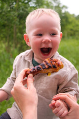 Laughing toddler outdoors with grilled chicken drumstick at picnic