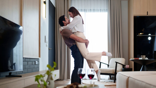 Romantic Asian Couple Embracing at Home with Red Wine Glasses Love and Intimacy in Modern Living Room Celebrating Anniversary Together - Powered by Adobe