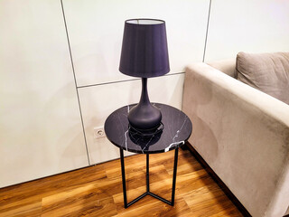 Modern black table lamp on a round black marble side table beside a beige sofa in a contemporary...