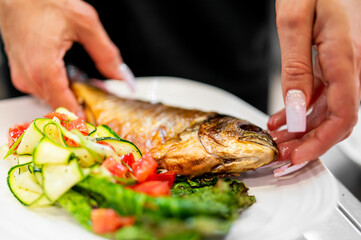 Whole grilled fish plated on a white dish with fresh zucchini and tomato salad. A healthy, colorful meal showcasing fresh ingredients and culinary presentation.