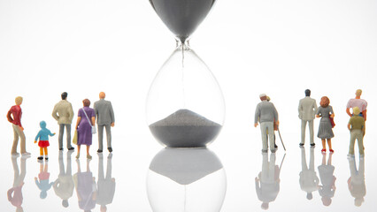 Small figurines representing a diverse group, observing a giant hourglass with flowing sand on a...