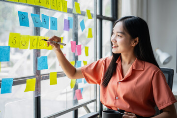 A woman is writing on a board with yellow and pink post it notes