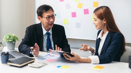 A man and a woman are sitting at a desk with a white board behind them