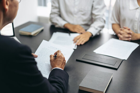 A man is writing on a piece of paper in front of a table with three other people
