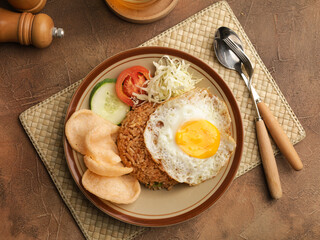 Fried rice with fried egg, vegetable salad and crackers on brown plate