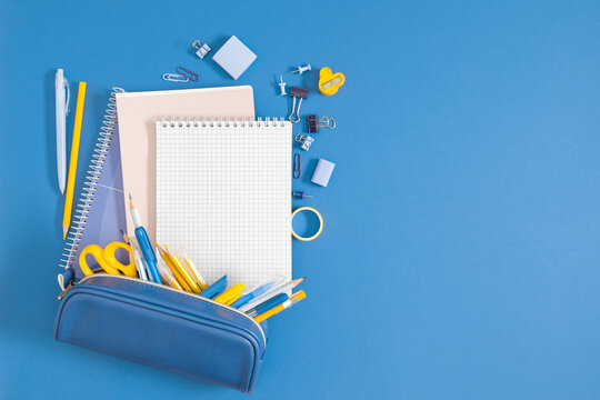 Back to school concept on blue background. Various school stationery items with a pencil case and notebook, as well as a sharpener, paper clips, tape, top view