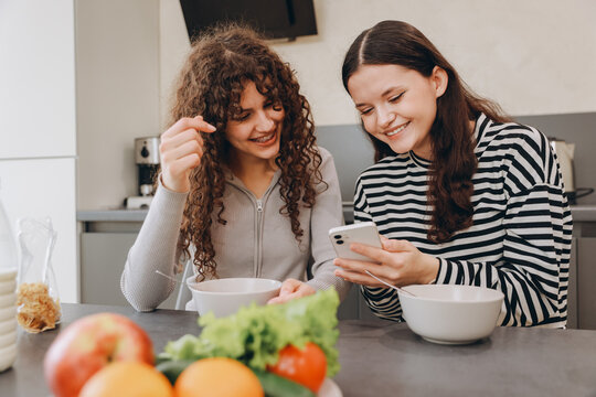 Teenage girls having breakfast and using smartphone in kitchen
