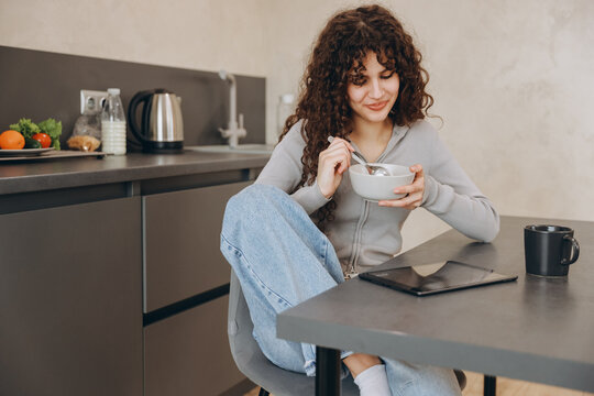 Young woman enjoying breakfast and using tablet in modern kitchen