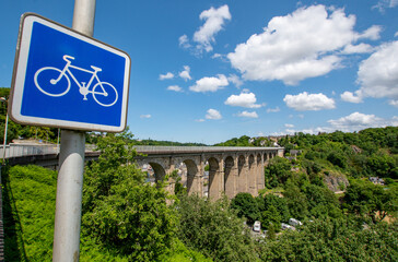 Cycling holiday in France image with a blue Cycle path sign in sharp focus and the iconic Dinan...