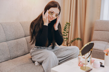 Obraz premium Teenager applying golden eye patches at home sitting on sofa