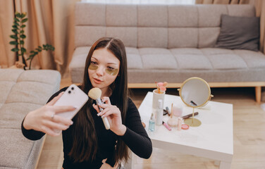 Beauty blogger applying makeup and recording tutorial for social media using smartphone at home