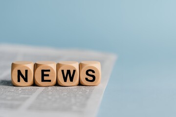 Wooden blocks spelling NEWS on a newspaper, concept for media, journalism, and communication