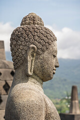 Closeup profile view of ancient Vairocana buddha statue in situ at historic Borobudur stupa, Magelang, Central Java, Indonesia