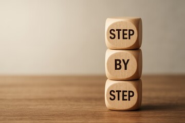 Three wooden cubes stacked on a light brown wooden surface, spelling out 'STEP BY STEP'; concept for business strategy, process, planning, and step-by-step instructions