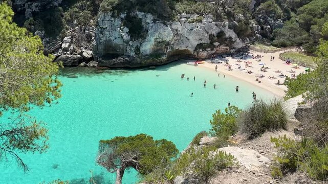 Cala Macarelleta beach in Menorca with clear turquoise water, golden sand and lush greenery.