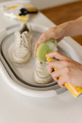 Close-up male hands cleaning pair of dirty white shoes in foldable basin using brush and cleaning foam, taking care of footwear hygiene and maintenance, closeup. Leather footwear care concept.