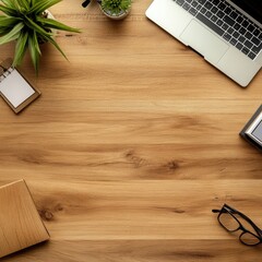 Overhead view of a minimalist workspace with a laptop, plants, stationery, and glasses on a light wood desk