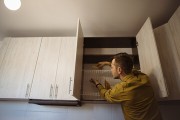Man arranging dishes in kitchen cabinet after moving into new house
