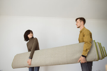 Couple carrying rolled up carpet moving into new apartment