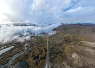 A long, straight road extends into the distance, surrounded by a vast and misty landscape with scattered water bodies and distant mountains