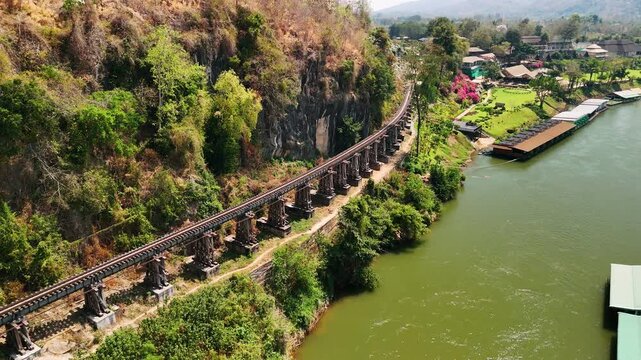 Wooden railway bridge along scenic river kwai, tracing historic Burma railway path through lush tropical landscape in Banchanaburi, Thailand.