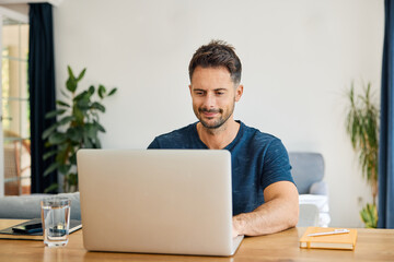Man working remotely on laptop at home office sitting at living room