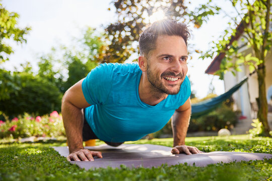 Smiling man doing pushups in the backyard garden