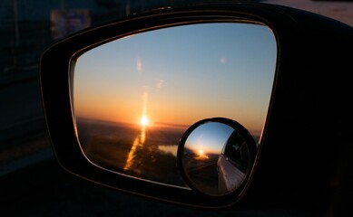 The dawn over the river is visible in the double rear-view mirror of the car.