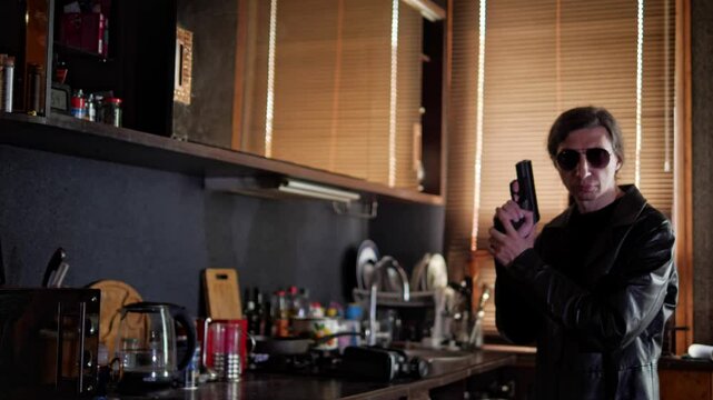 A mid-shot captures a serious and action-movie mood as a man in a leather jacket and sunglasses holds a handgun, aiming it directly forward, in a kitchen setting