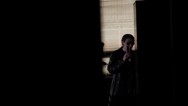 A dramatic mid-shot captures a mysterious and tense mood as a person in a leather jacket and sunglasses holds a handgun, partially hidden in shadow, operation or surveillant suggesting
