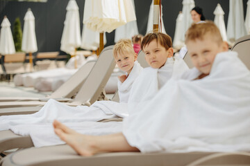 Children relaxing in bathrobes on lounge chairs at water park