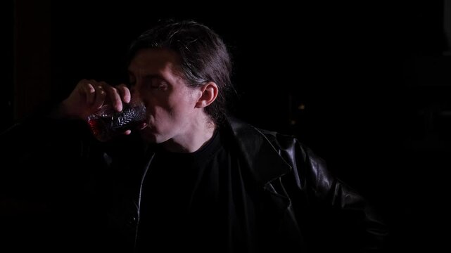A close-up shot captures a contemplative and solitary mood as a man in a dark leather jacket drinks from a glass, with his eyes closed, against a dark background, suggesting a private moment or escape