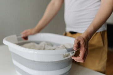 Professional housekeeper male holding white plastic basin brimming with soiled white linens, ready...