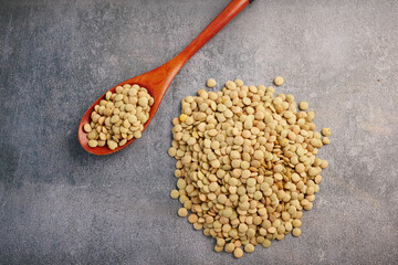 Green lentils spread on a surface with a wooden spoon nearby