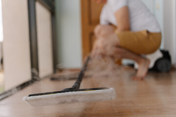 Man cleaning parquet floor with steam mop, visible vapor rising as surface becomes perfectly clean and disinfected, close-up. Concept of ensuring hygiene and healthy home environment