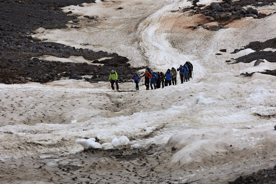 A Group Of Mountaineers With Backpacks And Trekking Poles Ascending A Steep Snowy Slope In A Mountainous Region.