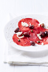 Slices of beef carpaccio with olives and capers. Close up.	