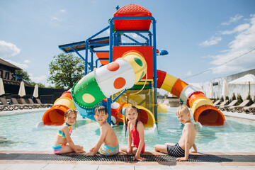 Happy children sitting by the colorful water slides at the poolside of water park