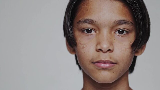 Close-up portrait of an Asian teenage boy with imperfect skin, looking confidently and naturally at the camera. A sincere and relatable image that highlights real beauty, adolescence, individuality