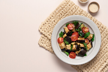 Eggplants tomatoes arugula salad in gray bowl on light beige background. Vegetarian summer Mediterranean salad