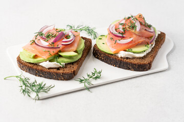 Smoked salmon avocado sandwich on light background. Black whole grain bread, avocado, salted salmon and dill for healthy breakfast