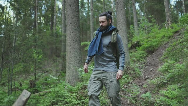 A survivalist walks down to a river in the forest to build a camp.