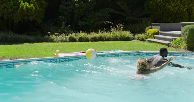 Diverse family of four sprinting across yard toward pool carrying float ring seeking refreshment